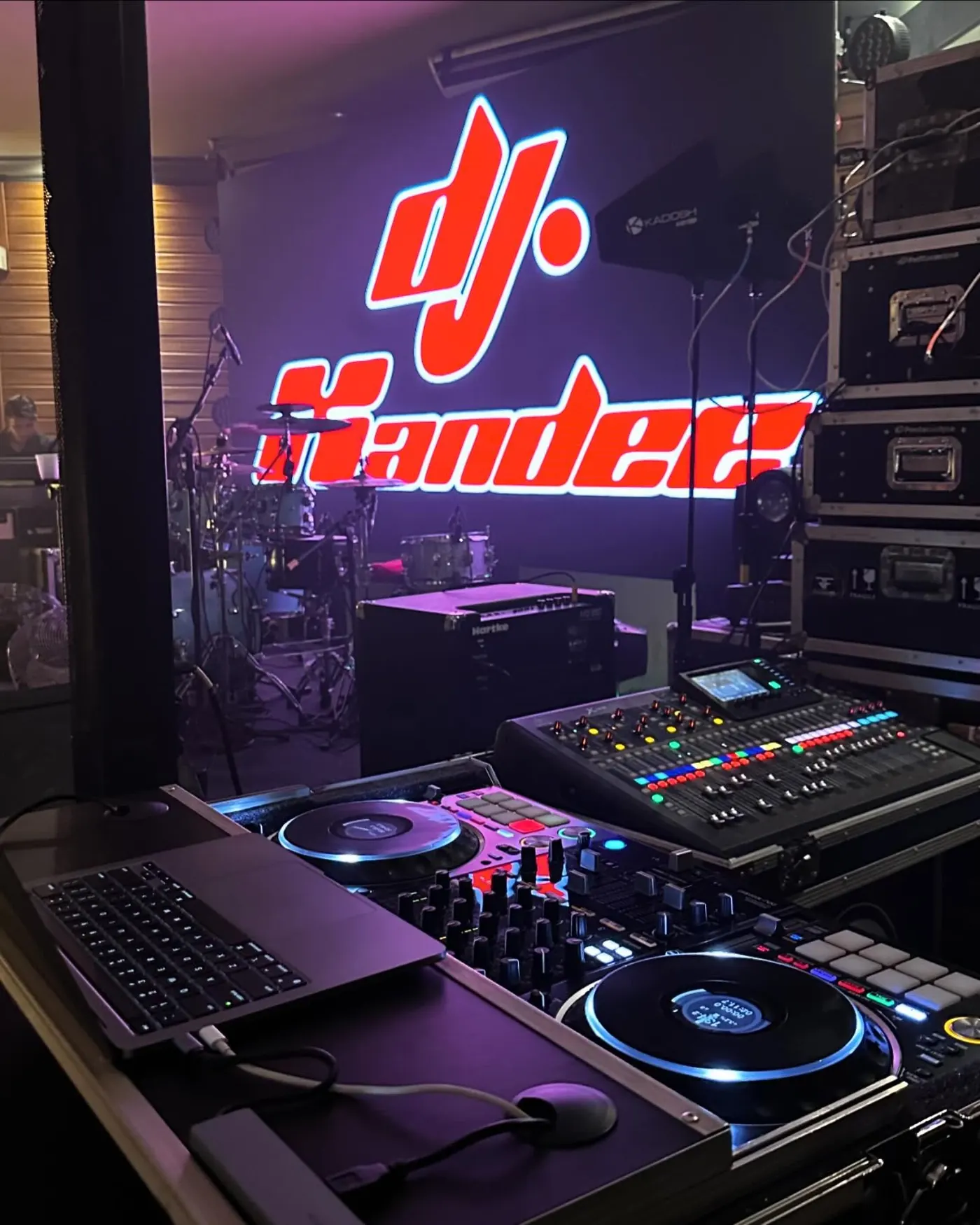 Cabine de DJ com mesa digital e a logo DJ Xandee no painel de LED